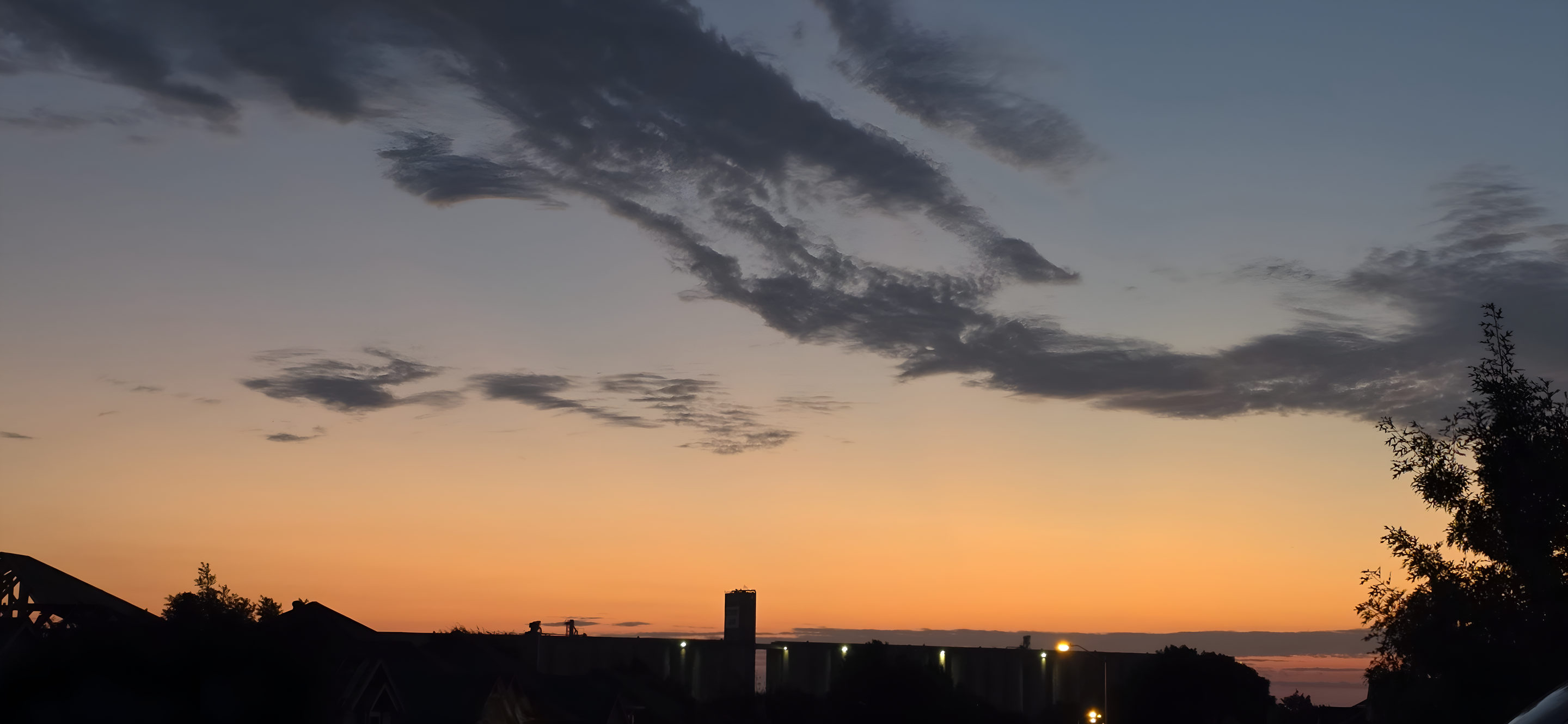 Dawn over the Attebury grain elevator in Saginaw, Texas, a blue sky streaked with cloud above an orange horizon and the dark silhouette of the elevator and rooftops